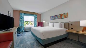 Una habitación de hotel con cama, escritorio, silla, televisor y ventana con cortinas.