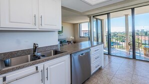Une cuisine moderne avec des meubles blancs, des appareils en acier inoxydable et une grande fenêtre donnant sur un balcon avec vue sur la ville.