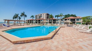 A swimming pool with lounge chairs, a thatched-roof structure, and a multi-story building with balconies. - PA C-401 - Palma - Standard Plus (St. Petersburg)