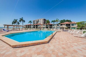 A swimming pool with lounge chairs, a thatched-roof structure, and a multi-story building with balconies. - PA C-401 - Palma - Standard Plus (St. Petersburg)