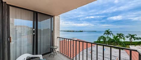 A balcony with a view of the sea, a table, and two chairs.