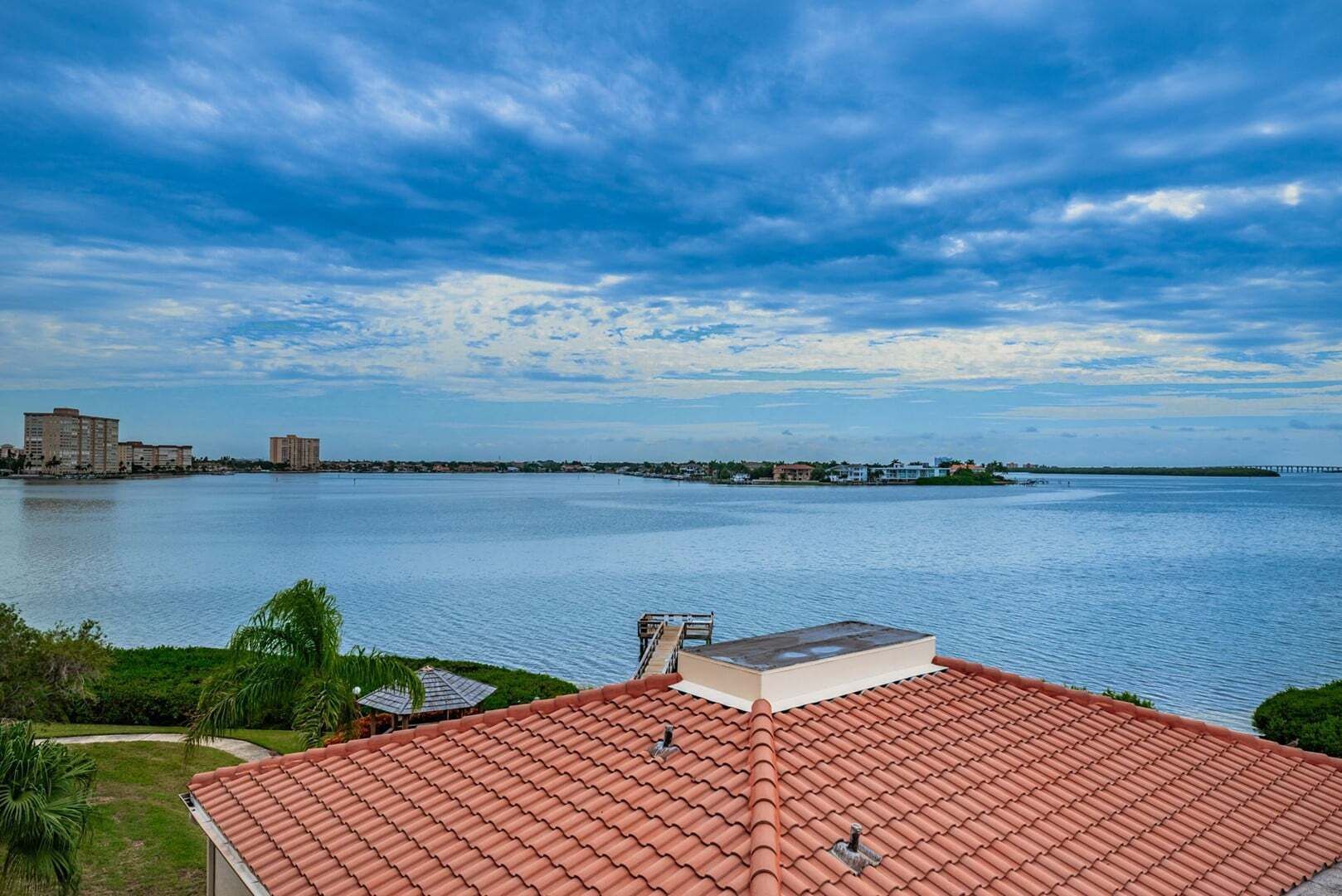 A coastal view with a red-tiled roof, a body of water, and distant buildings.