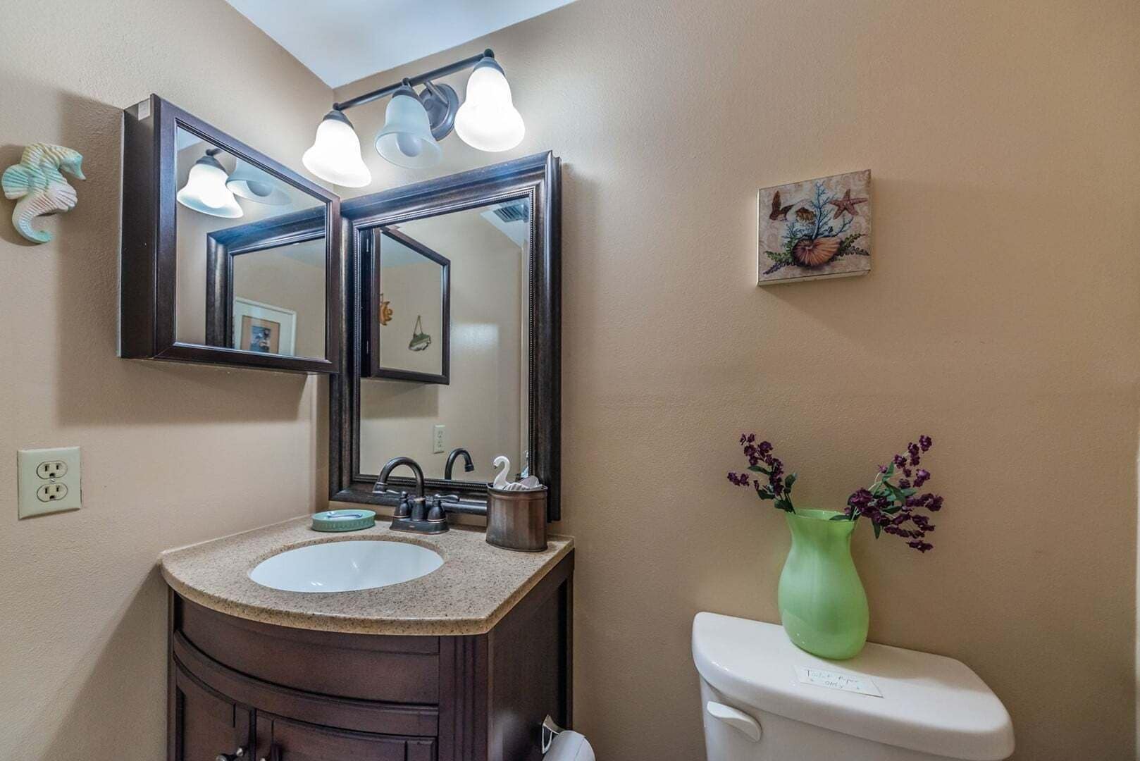A bathroom with a double vanity, a large mirror, a toilet, and a vase with flowers.
