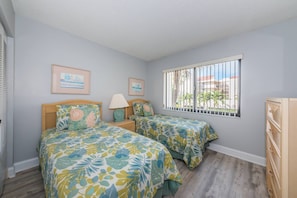 A bedroom with two beds, a window with bars, and a dresser.