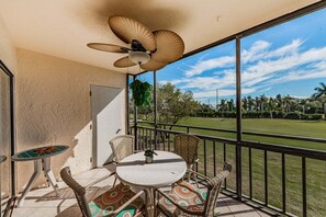 A balcony with a table and chairs, a ceiling fan, and a view of a golf course.