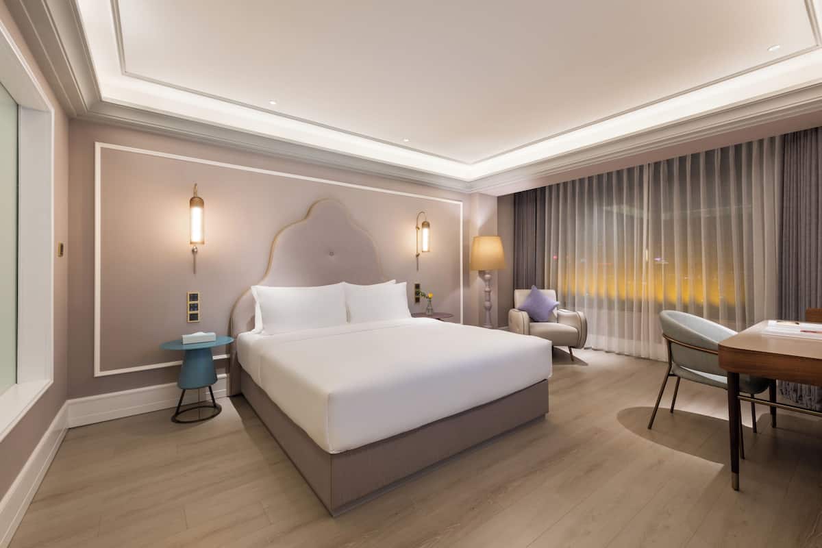 A modern hotel room with a large bed, a round table, a chair, and a desk.