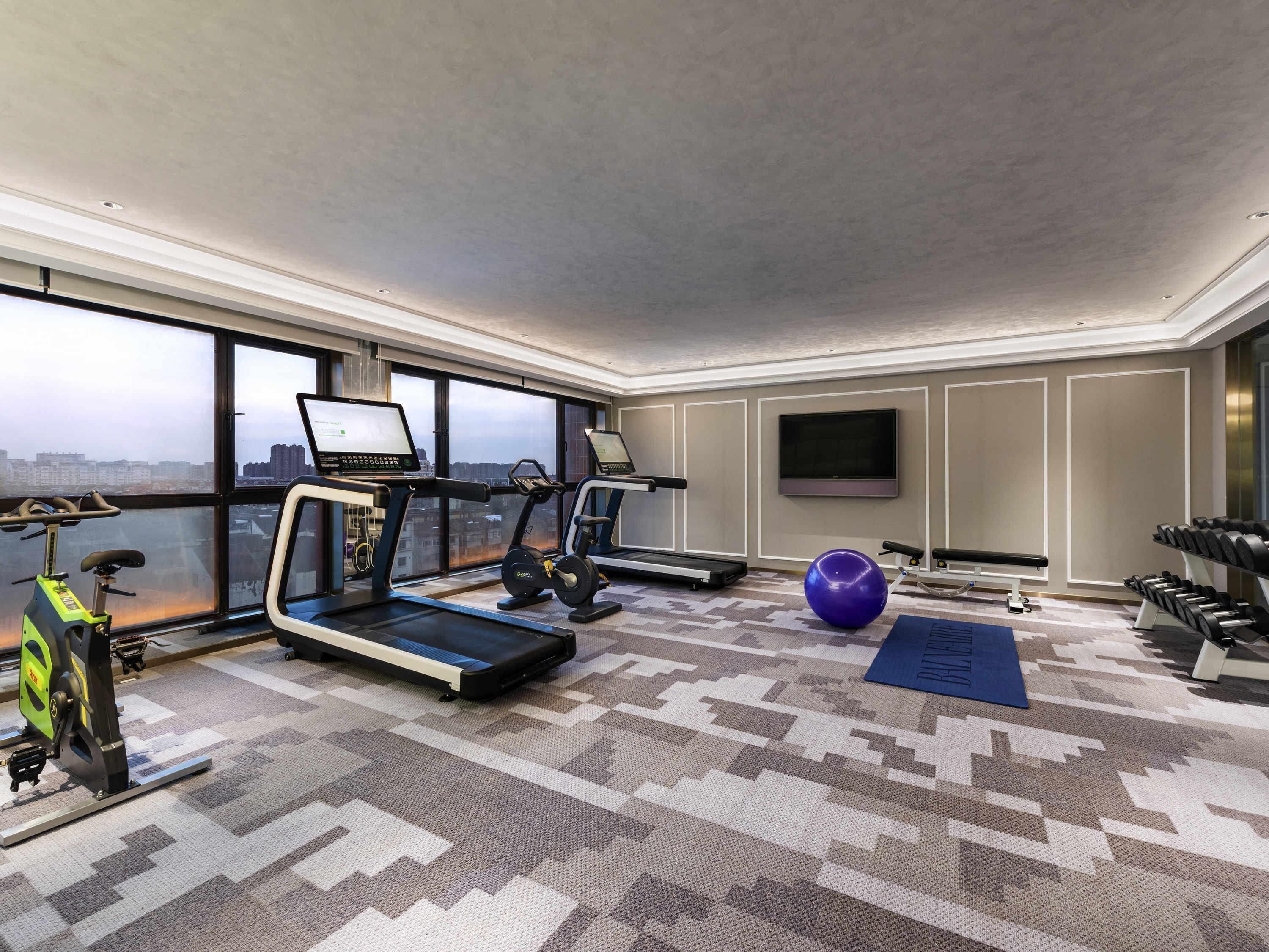 A modern gym with exercise equipment, a large window, and a city view.