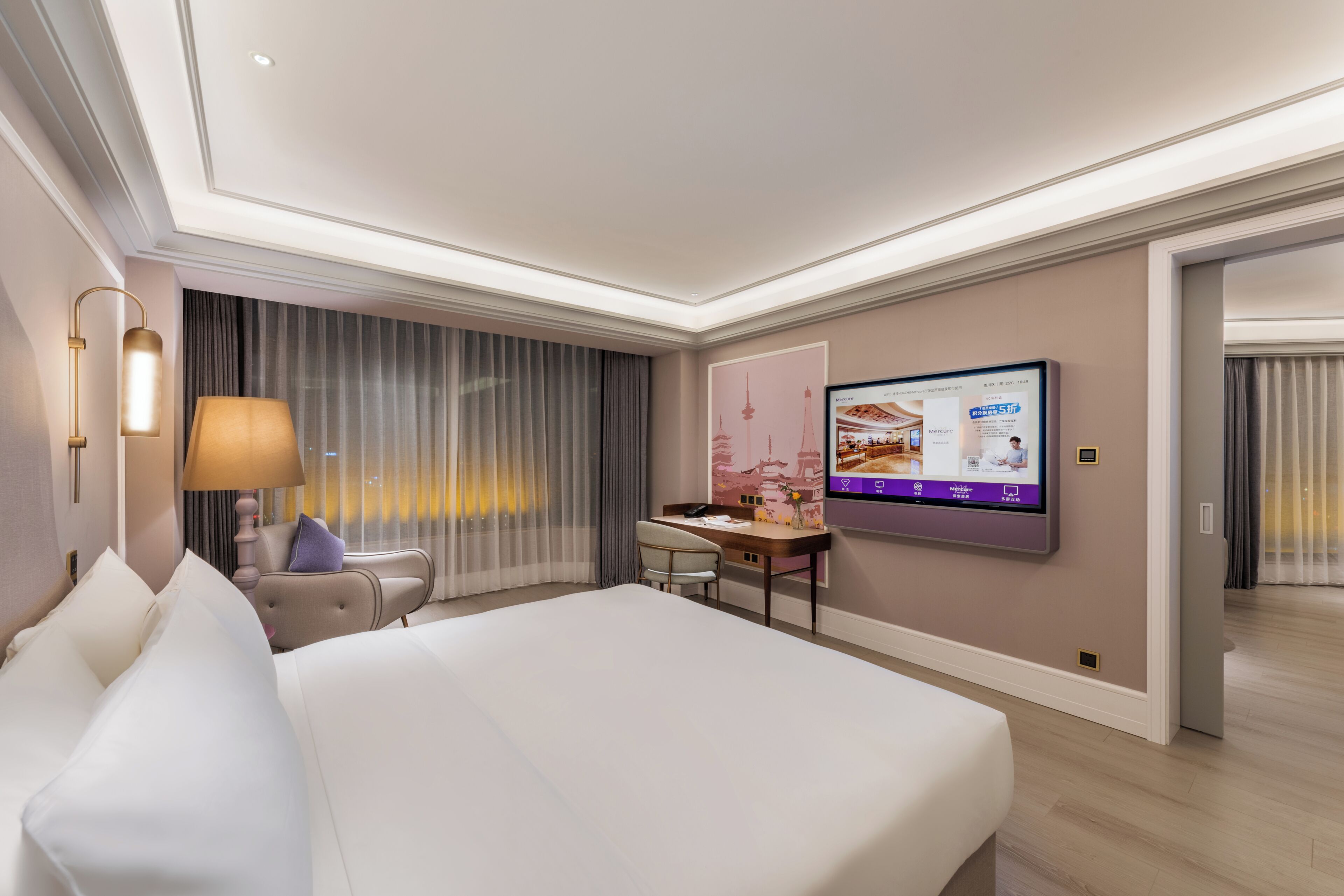 Une chambre d’hôtel équipée d’un lit, d’un bureau, d’une chaise, d’une télévision, de rideaux et d’un écran fixé au mur.