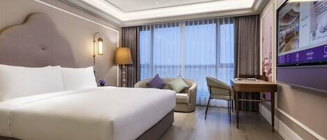 A hotel room with a large bed, a desk, a chair, a TV, and a view of the outdoors.