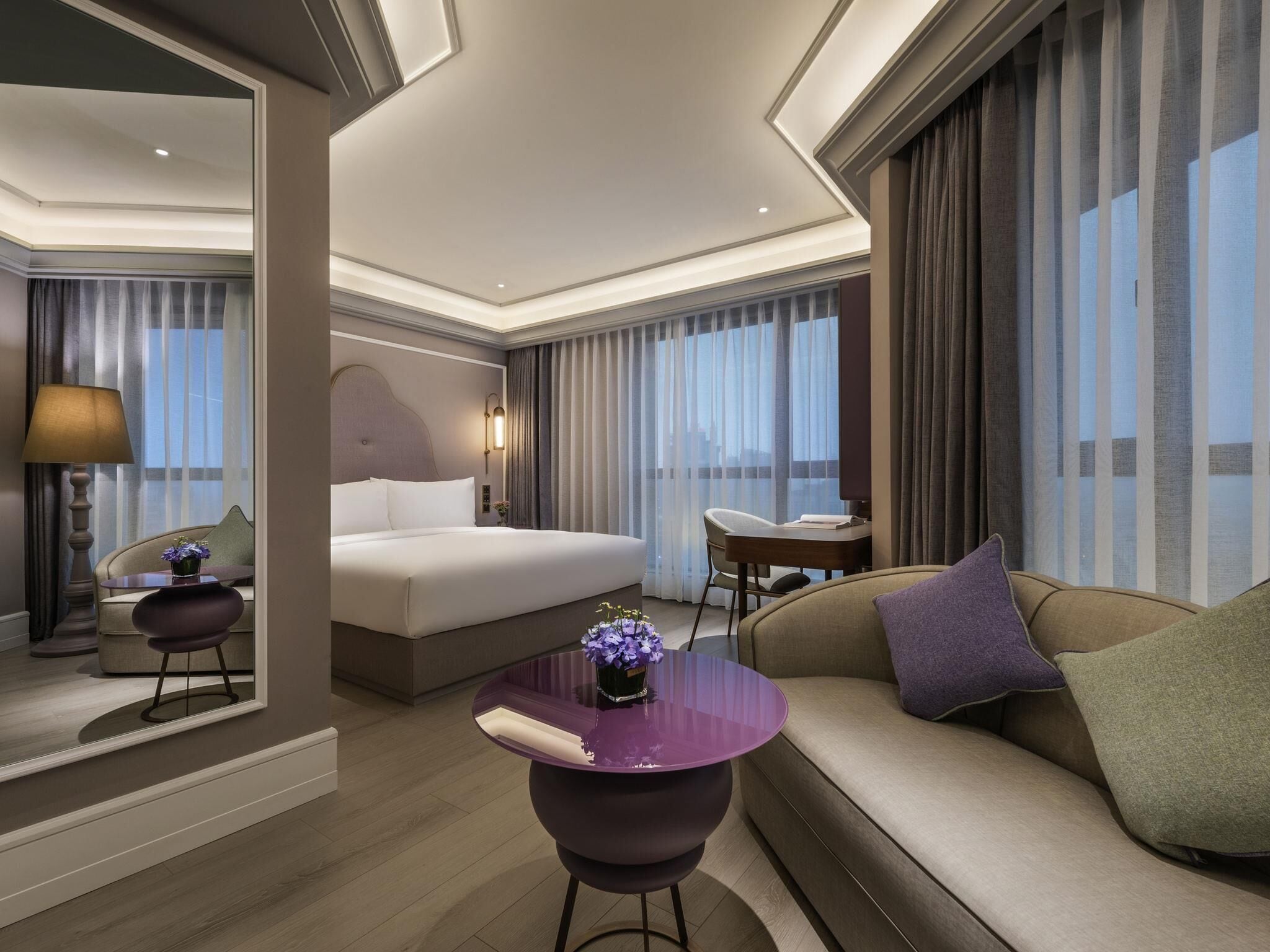 Une chambre d’hôtel moderne avec un grand lit, un canapé, un bureau et une vue sur la ville.