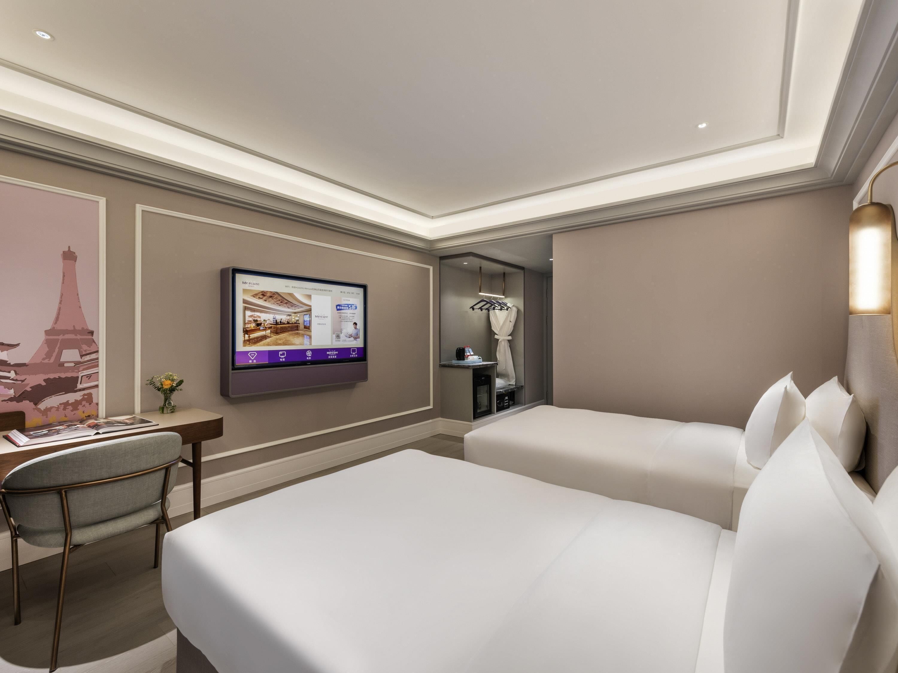 Une chambre d’hôtel comprenant un lit, un bureau, une chaise, un téléviseur à écran plat fixé au mur et un miroir.