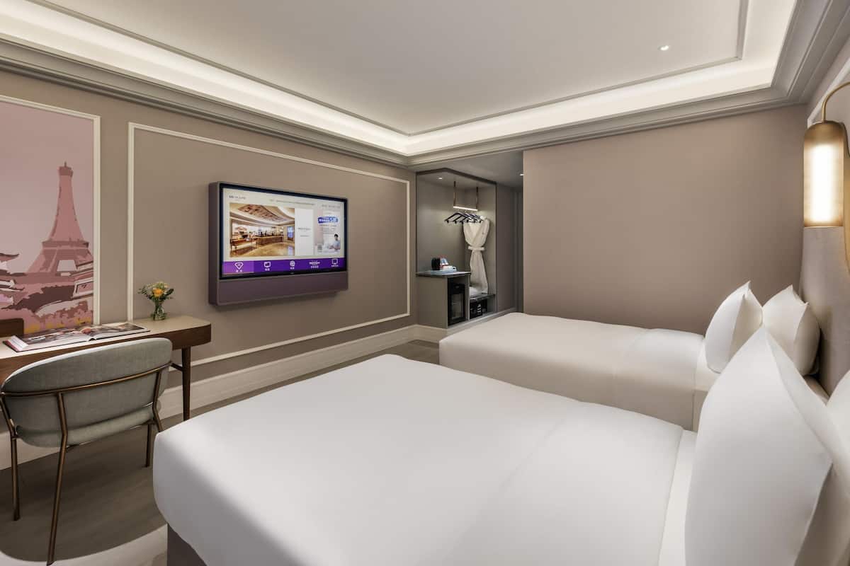 A hotel room with a bed, a desk, a chair, a flat-screen TV mounted on the wall, and a mirror.