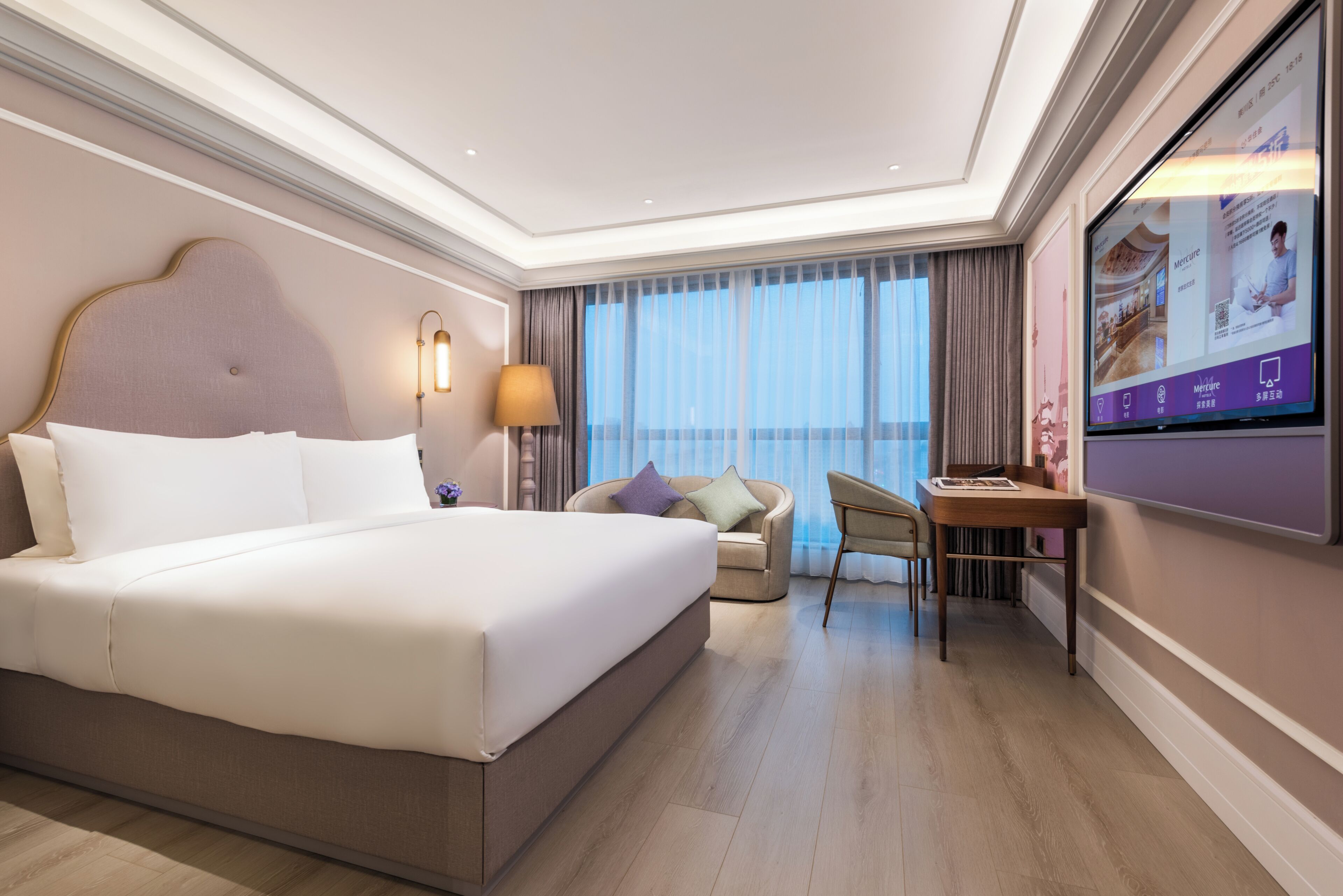 A hotel room with a large bed, a desk, a chair, and a TV on the wall.
