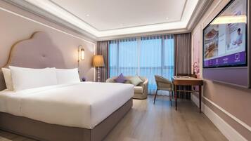 A hotel room with a large bed, a desk, a chair, and a TV on the wall.