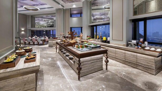 A spacious hotel lobby with a marble floor, a central bar area with a variety of food and drink options, and large windows offering a city view. - Mercure Nantong Downtown (Nantong)