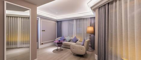 A modern hotel room with a sofa, a small side table, a lamp, and a large window with curtains.
