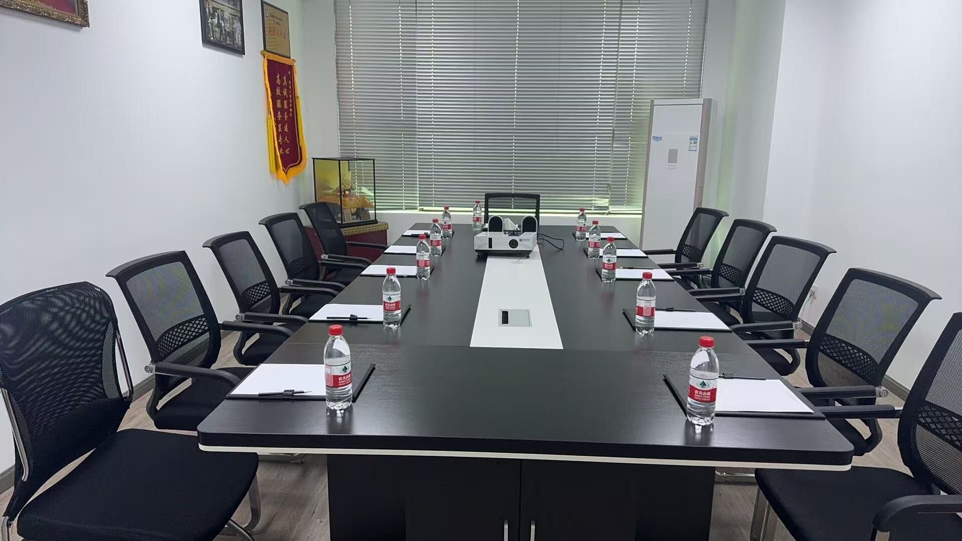 A conference room with a long table, black chairs, water bottles, and a projector.