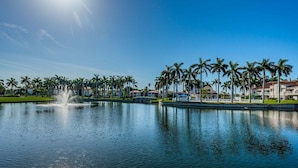 Un lago tranquilo con una fuente, rodeado de palmeras y edificios.