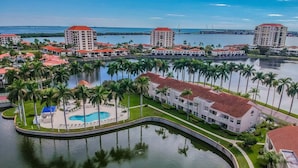Un resort con piscina central, palmeras y edificios con techos rojos.