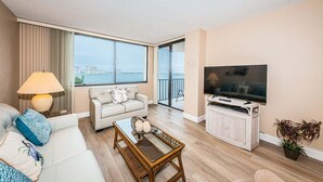 Een moderne woonkamer met een bank, salontafel en televisie, grote ramen met uitzicht en een balkon.