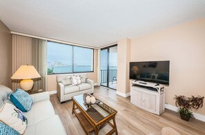 Ein modernes Wohnzimmer mit Sofa, Couchtisch und Fernseher, großen Fenstern mit Blick und einem Balkon.