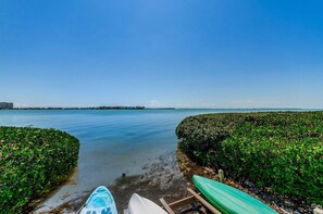 Vista de una playa con cielo despejado, agua tranquila y dos kayaks en la orilla.