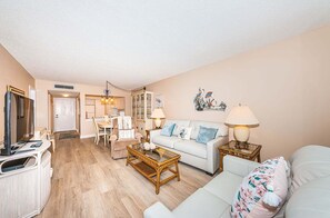 A living room with a sofa, coffee table, and lamps. There is a dining area with chairs and a table.