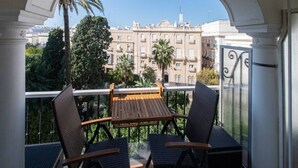 A balcony with two wicker chairs and a wooden table, overlooking a cityscape with buildings and palm trees. - Jardines de Candelaria Cadiz (Cádiz)