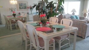 Un coin repas avec une table à plateau de verre, des chaises blanches et une grande plante en pot.