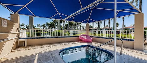 Un espace piscine agrémenté d’un auvent bleu, d’un fauteuil de relaxation rose et d’une vue sur des palmiers.