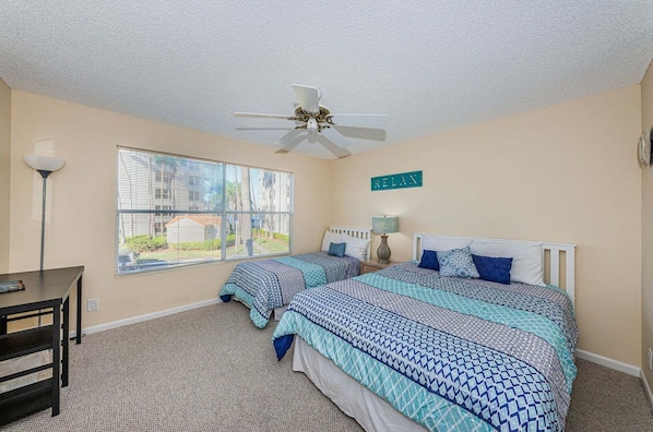 A bedroom with two beds, a ceiling fan, a desk, and a window with blinds.