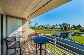 A balcony with wicker furniture and a view of a golf course and water feature.