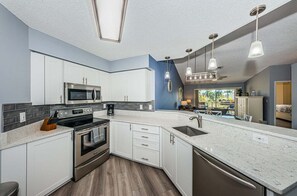 A modern kitchen with white cabinets, a stainless steel oven, and a large island with a sink. - VVW 6-236 - Vista Verde West - Premium (St. Petersburg)