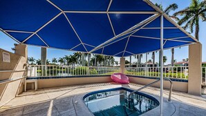 A pool area with a blue canopy, a pink lounge chair, and a view of palm trees. - VVW 6-138 - Vista Verde West - Standard (St Petersburg)