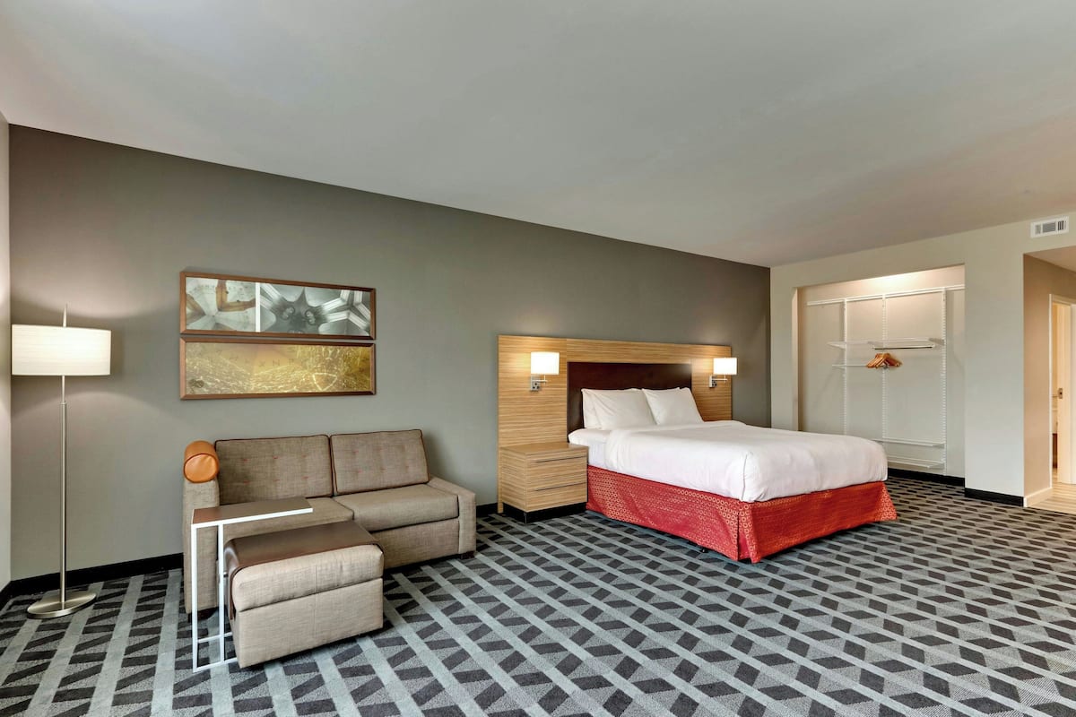 Une chambre d’hôtel comprenant un lit, un canapé, une table de chevet, une lampe et une œuvre d’art accrochée au mur.