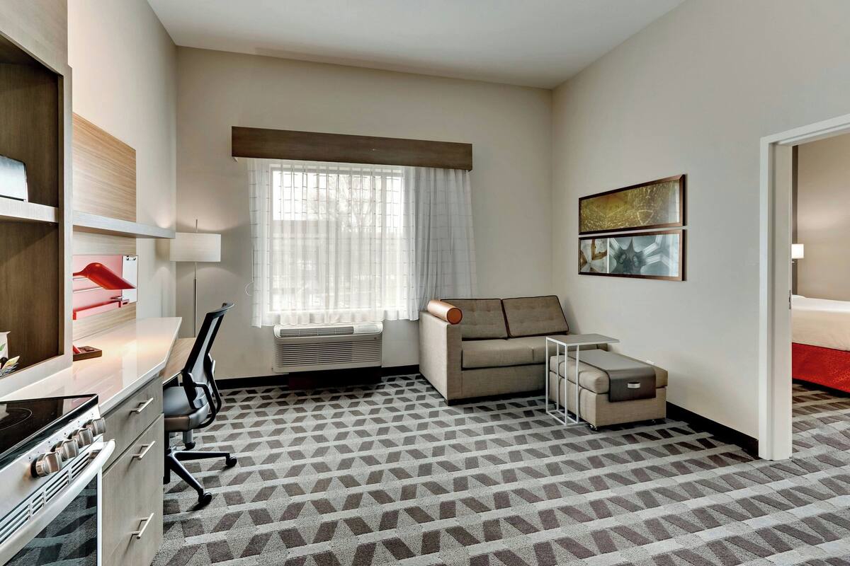 Une chambre d’hôtel équipée d’une kitchenette, d’un canapé, d’un bureau et d’une fenêtre avec des rideaux.