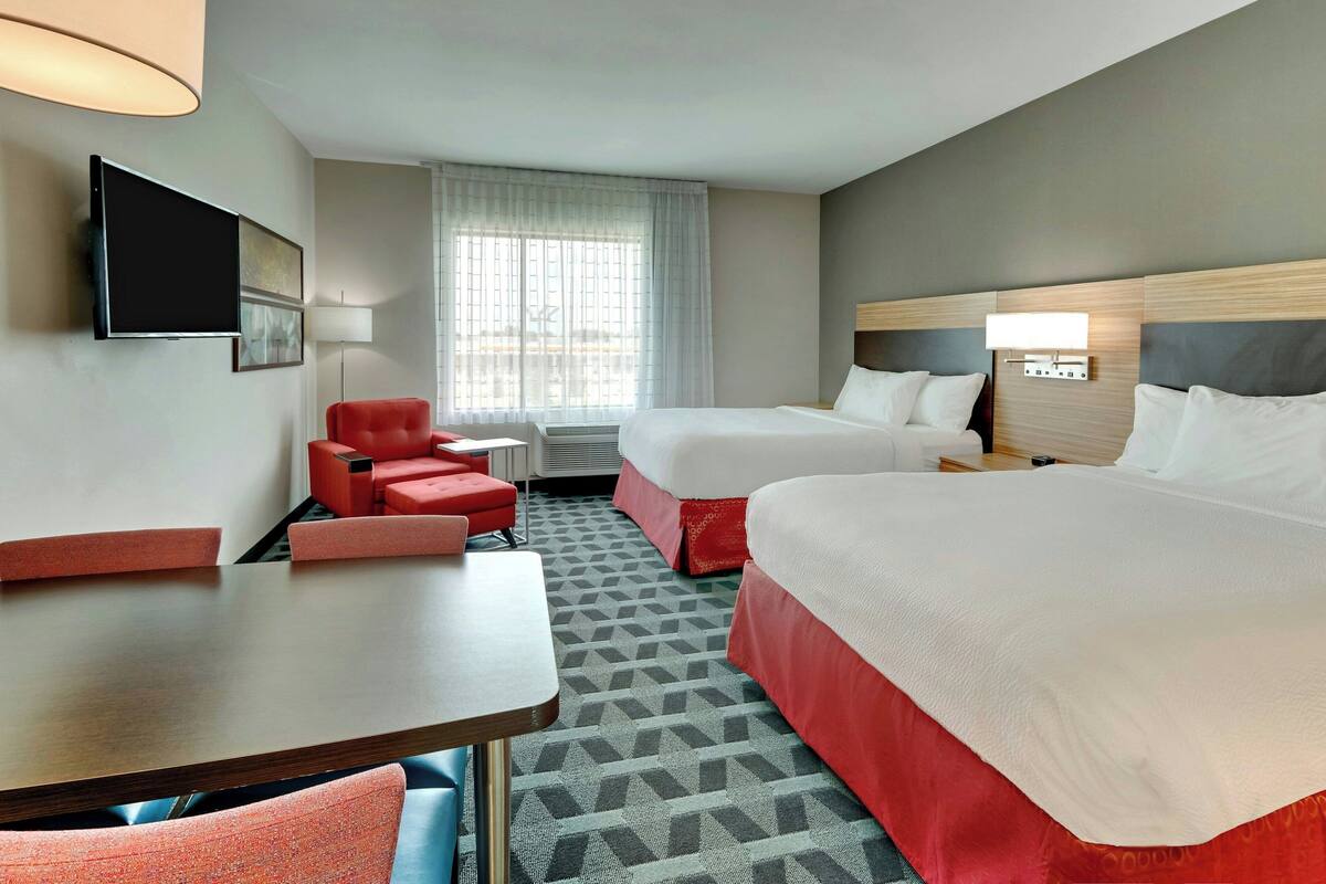 Une chambre d’hôtel avec deux lits, un bureau, une chaise, une télévision et une fenêtre avec des rideaux.