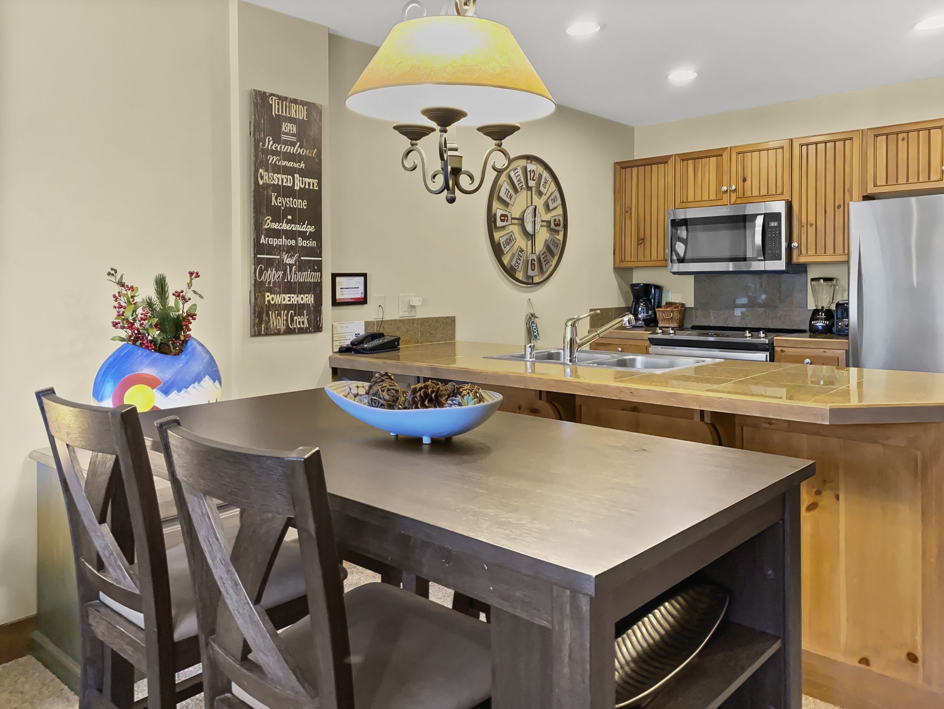 A modern kitchen with wooden cabinets, a central island with a sink, a microwave, and a refrigerator.