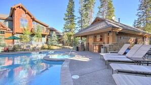 Un espace piscine avec des chaises longues, un coin barbecue et un bâtiment à la façade en pierre.