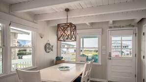 Ein Essbereich mit weißem Tisch und Stühlen, einer Hängeleuchte und Blick auf den Strand durch große Fenster.