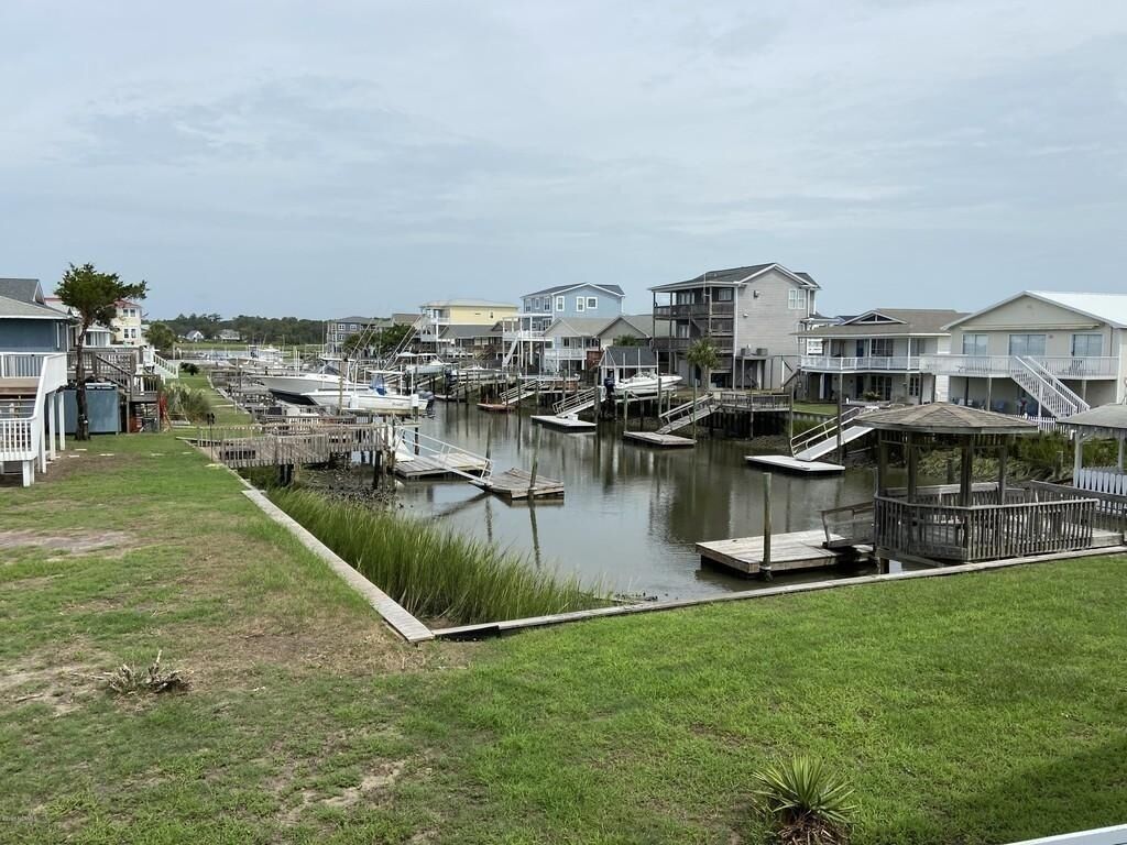 Un port de plaisance avec des bateaux amarrés, des maisons au bord de l’eau et une zone herbeuse.