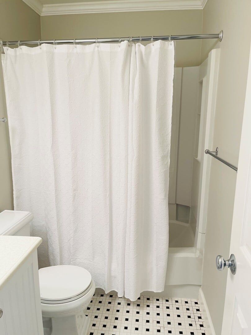Une salle de bain avec un rideau de douche blanc, des toilettes et un sol carrelé.