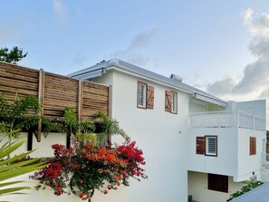 Ein modernes, zweistöckiges Gebäude mit weißer Fassade, Holzläden an den Fenstern und einem Balkon mit weißem Geländer.