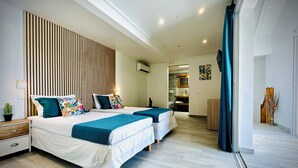 A modern hotel room with two beds, a wooden headboard, a small bedside table, a potted plant, and a view of the adjacent kitchen and balcony. - Villa Exotic Life, 2 bedrooms, heated pool (Le Moule)
