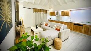 A modern living room with a sofa, coffee table, and a dining area with wooden cabinets and a kitchen island. - Villa Exotic Life, 2 bedrooms, heated pool (Le Moule)