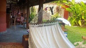 Eine Hängematte unter einer Holzw pergola in einem Gartenbereich mit einem gemusterten Teppich, einem Tisch mit Stühlen und einer Wand mit hängender Dekoration.