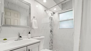 A modern bathroom with a white marble sink, a toilet, and a shower with a glass door. - Luxury Beach Condo Getaway with fast Wifi (Lake Worth)