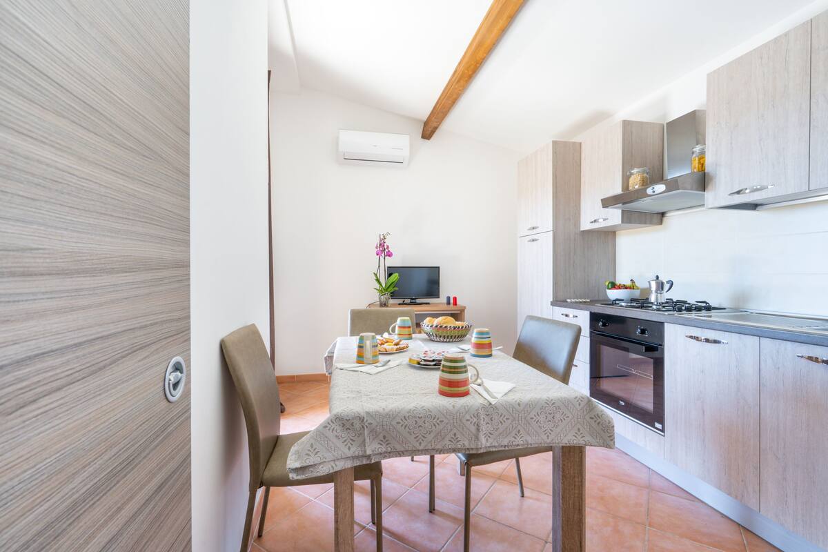 A compact kitchen with wooden cabinets, a dining table set with plates and cups, and a television in the background.