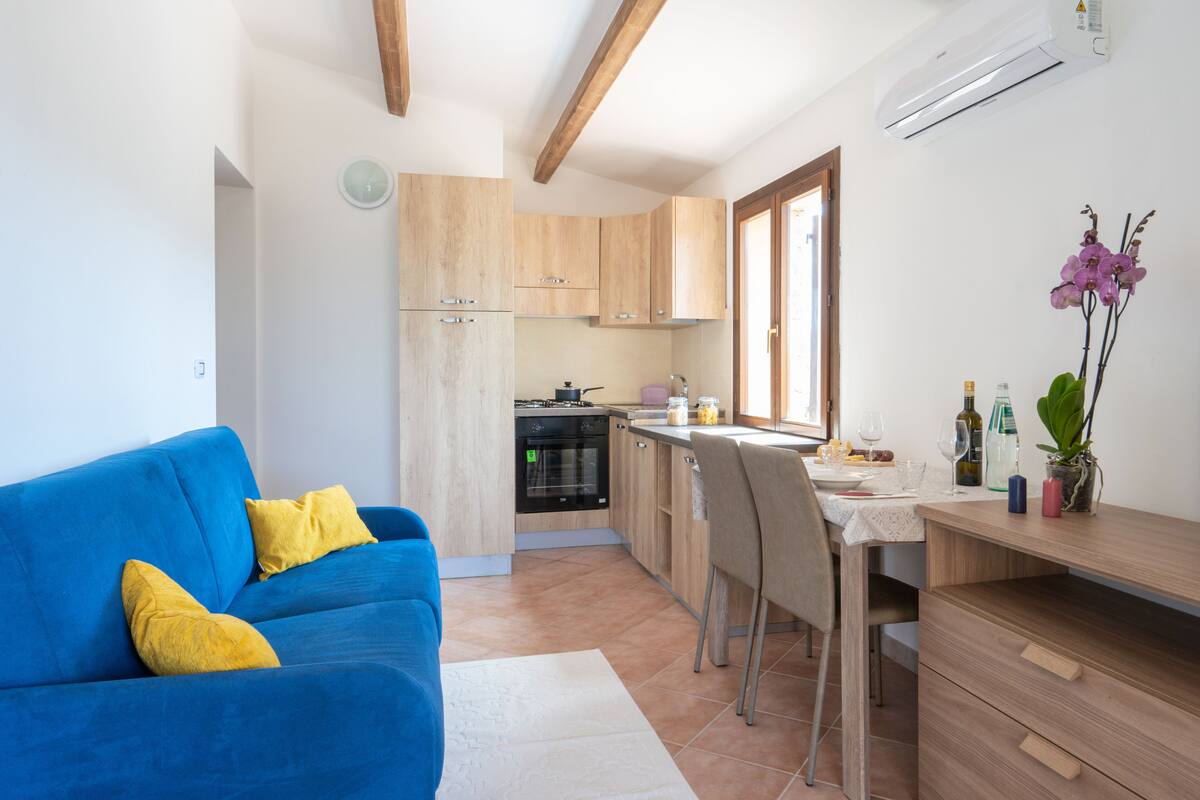 A modern kitchen with wooden cabinets, a dining area with a table and chairs, and a blue sofa with yellow cushions.