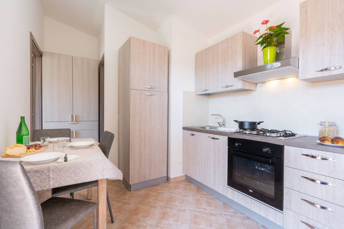A compact kitchen with a dining area, featuring a stove, oven, and a small shelf with a plant.